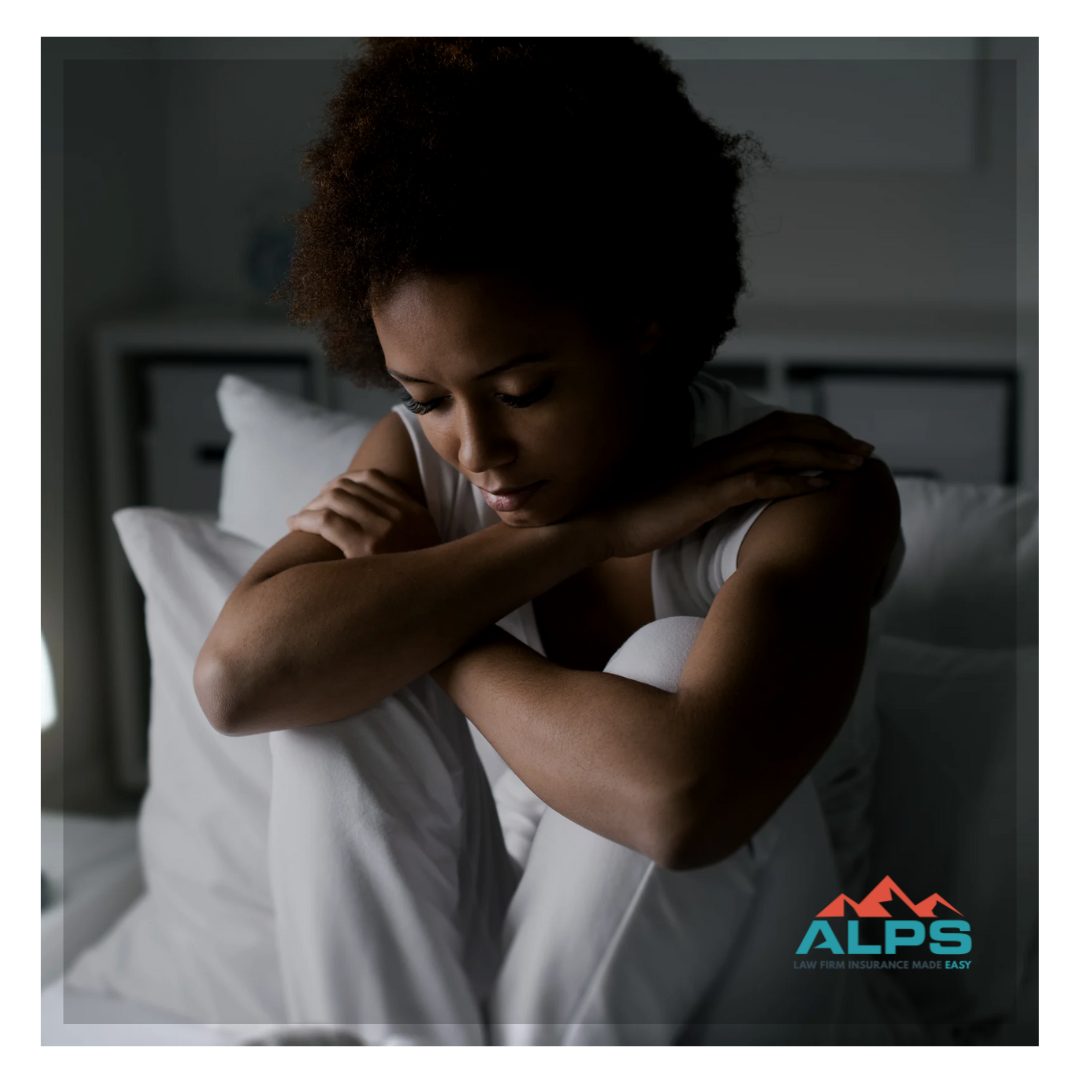 Sad woman sitting on her bed with her knees up to her chest and her arms wrapped around her knees.
