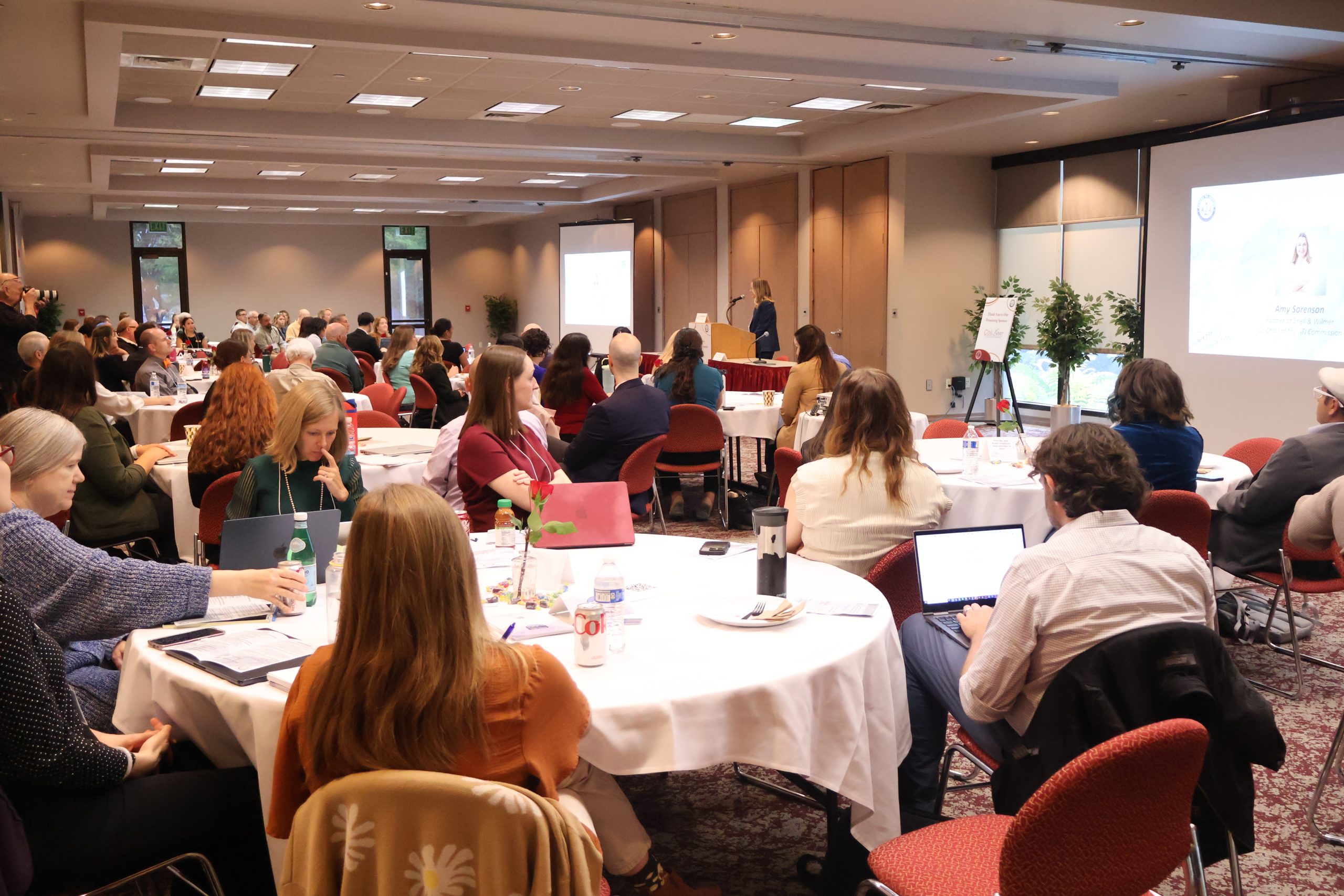 Amy Sorenson gives the keynote address from a podium in front of a crowd of more than 100 seated participants at round tables at the Utah Law & Justice Center